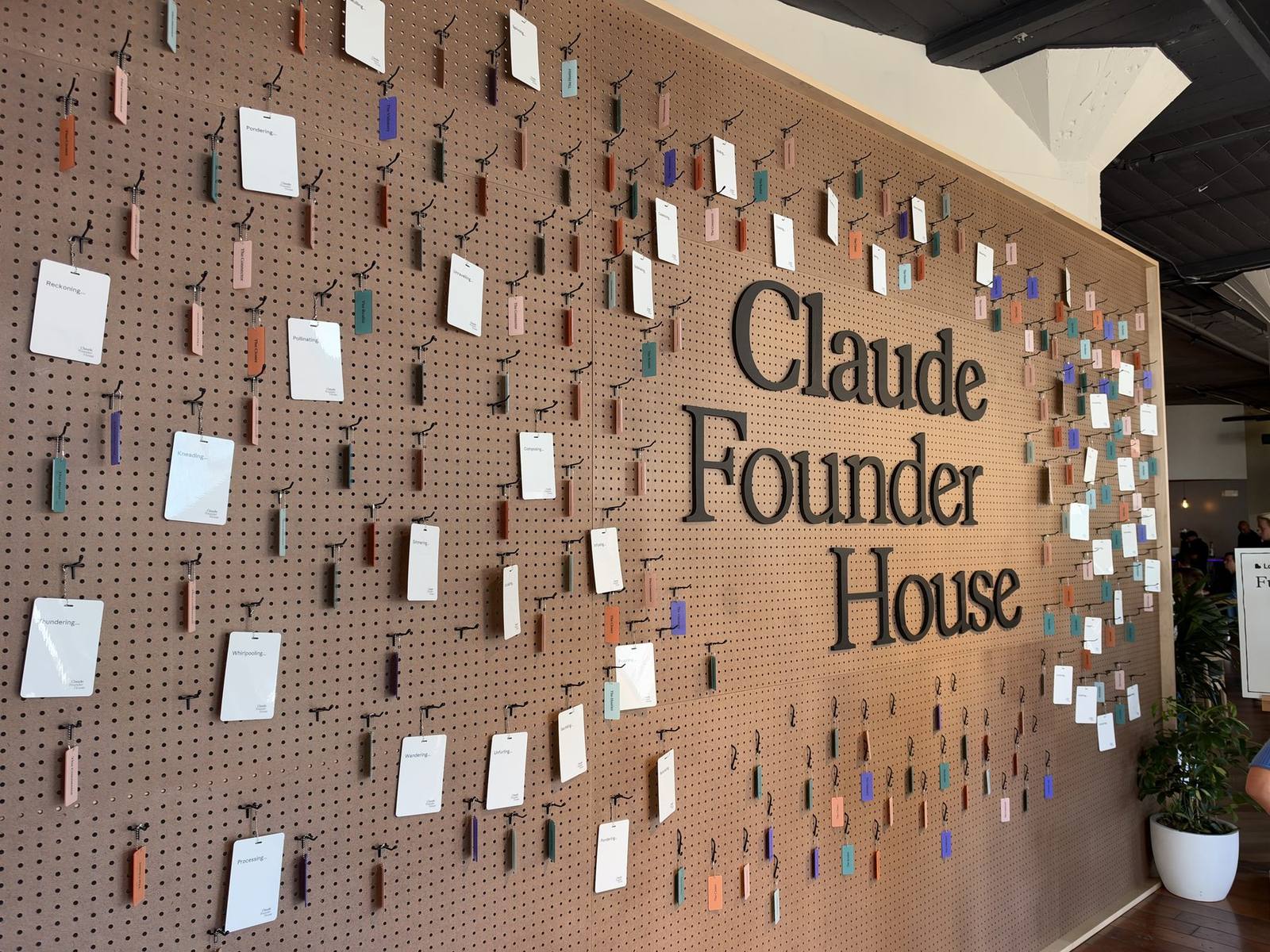 The Claude Founder House wall in San Francisco, with the event name in large letters on a pegboard covered in hanging name tags.